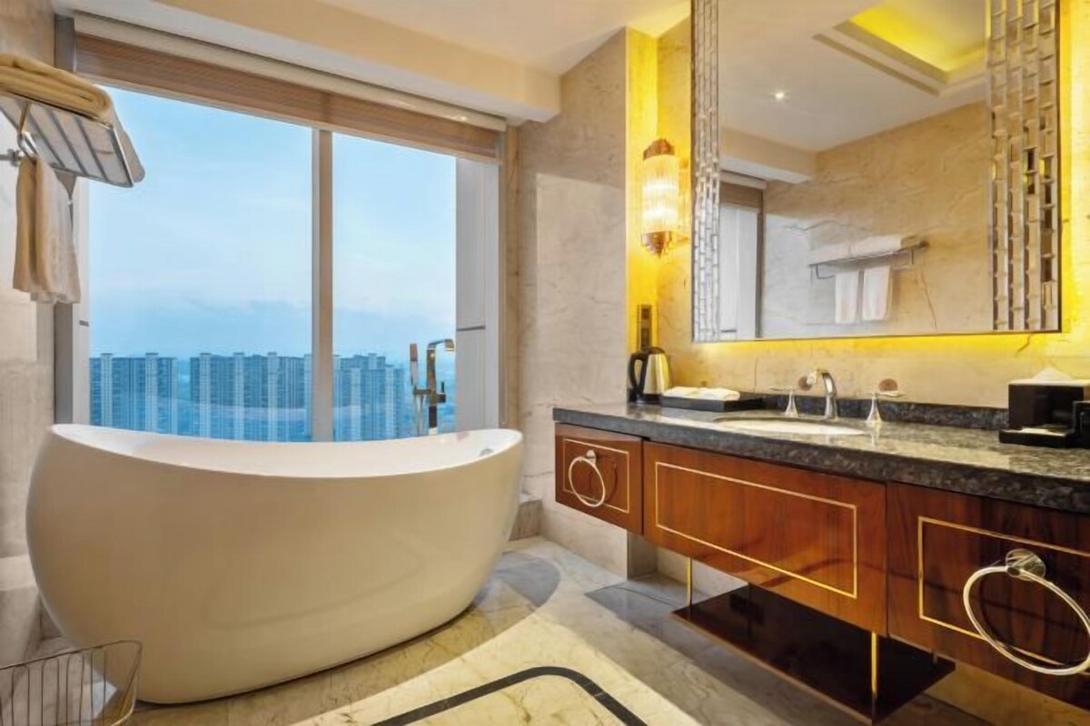 Une salle de bain moderne avec une baignoire sur pieds, un grand miroir et une vue sur le paysage urbain, visible à travers une grande fenêtre.