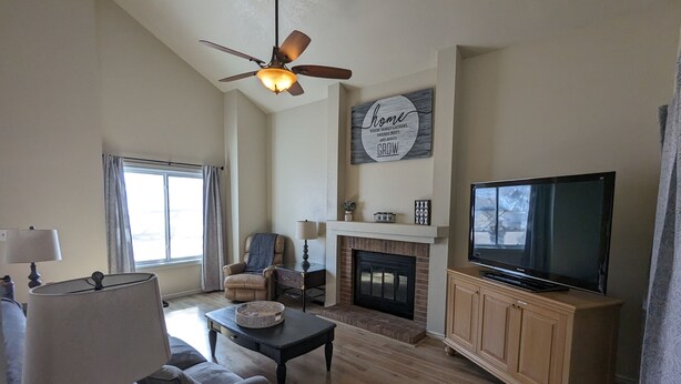 A living room with a fireplace, a television, a ceiling fan, and a large window. - Pet Friendly, Mountain View Home with Park/Playground Access  *see description* (Colorado Springs)