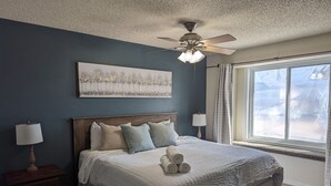 A bedroom with a large bed, a ceiling fan, a window with curtains, and a nightstand with a lamp. - Pet Friendly, Mountain View Home with Park/Playground Access  *see description* (Colorado Springs)