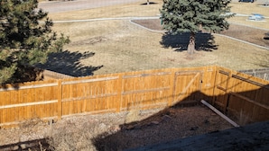 A residential area with a wooden fence, a grassy yard, and a tree. - Pet Friendly, Mountain View Home with Park/Playground Access  *see description* (Colorado Springs)