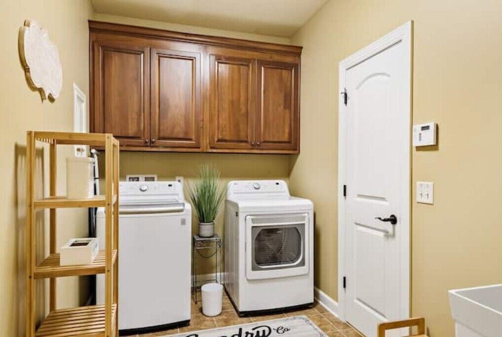 A laundry room with two white washing machines, a wooden cabinet, and a door.
