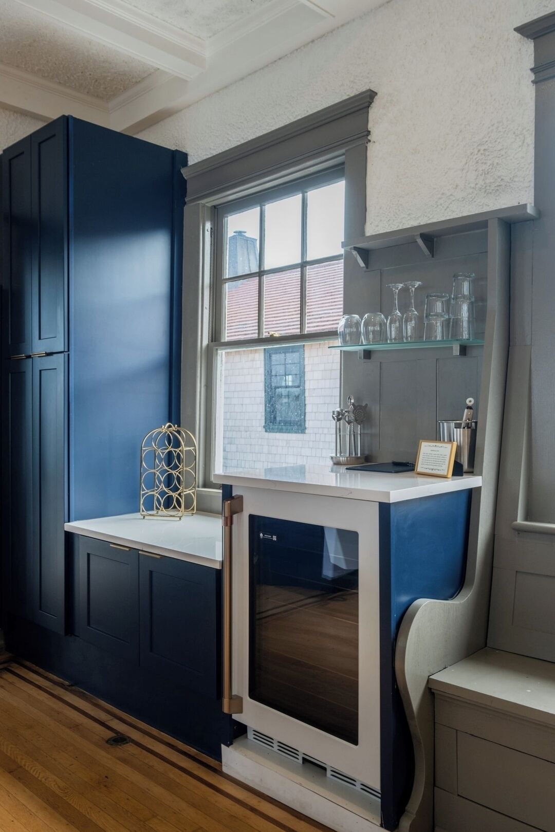 Una cocina con armarios azul oscuro, una encimera blanca y una ventana con vista a un edificio de ladrillo.