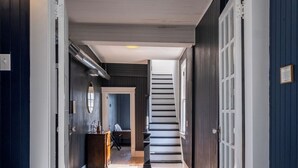A hallway with a patterned rug, wooden flooring, and a staircase leading to another room. - The Capone House | Historic Luxury on the Bay (Atlantic City)