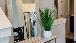 A mirror with a textured frame, a potted plant, and a glimpse of a kitchen area. - 3-Story Downtown Houston Safe Haven (Houston)