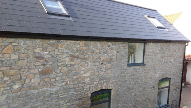 A stone building with a sloped roof, two skylights, and two windows.
