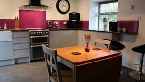 A modern kitchen with a wooden table, two chairs, a stove, and a clock on the wall.