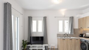Moderni keittiö, jossa on sisäänrakennettu pesukone, valkoisella jalustalla oleva televisio ja pieni pyöreä pöytä.