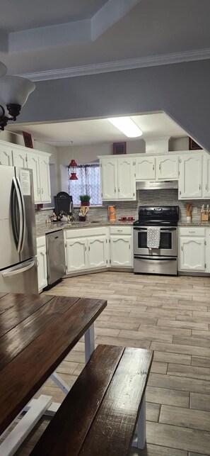 A kitchen with white cabinets, a stainless steel refrigerator, a black stove, and a wooden table.