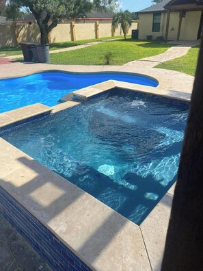 En swimmingpool med en kant av kakel, en gräsyta och en byggnad i bakgrunden.
