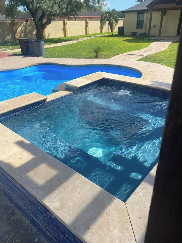A swimming pool with a tiled edge, a grassy yard, and a building in the background.