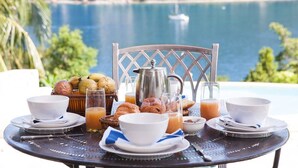 A breakfast table with croissants, fruit, and coffee, overlooking a scenic ocean view.