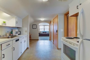 A narrow kitchen with white cabinets, a stove, and a dining area visible in the background.
