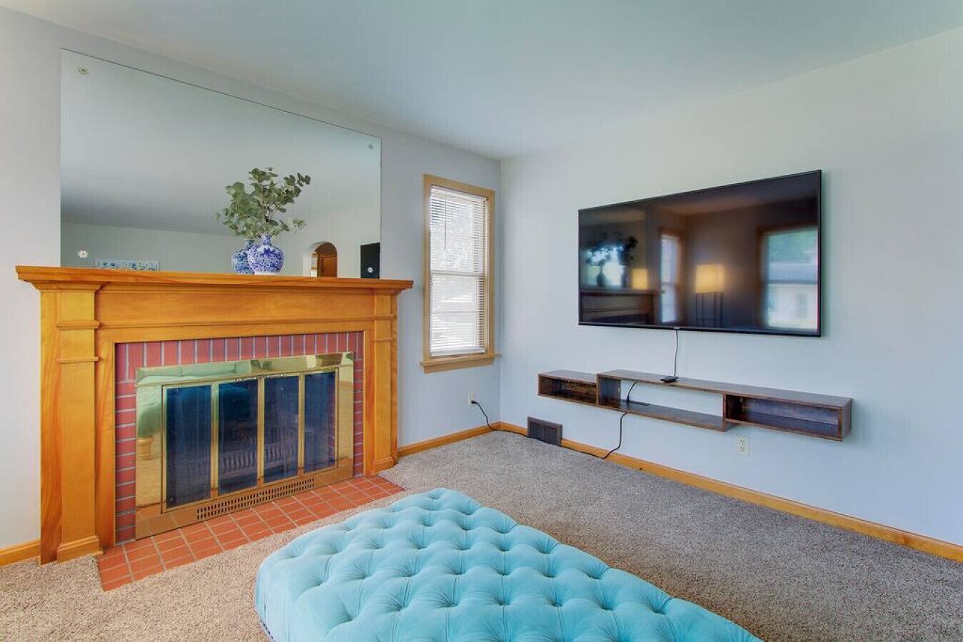A living room with a fireplace, a television mounted on the wall, and a blue ottoman.