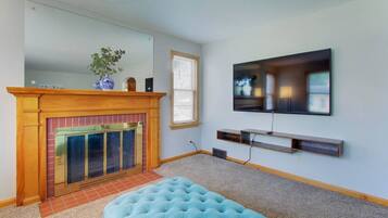 A living room with a fireplace, a television mounted on the wall, and a blue ottoman.