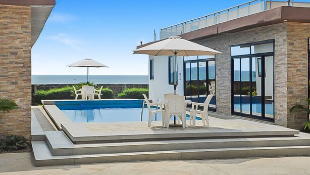 A modern outdoor pool area with a view of the ocean, surrounded by stone walls and furnished with white chairs and umbrellas. - 2 Bed/2.5 Bath Villa (Lewa) (Monrovia)
