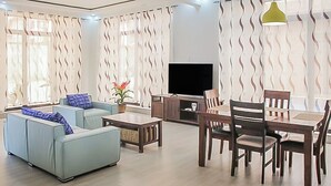 A modern living room with a sofa, coffee table, dining table, chairs, and a TV.