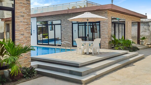 A modern pool area with a glass-enclosed pool, outdoor seating, and a staircase leading to a covered patio.