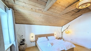 Een slaapkamer met een houten plafond, een bed met witte lakens, een potplant en wandlampen.