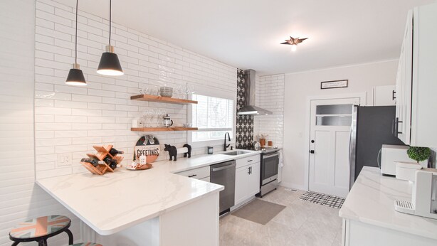 Una cocina moderna con azulejos blancos tipo metro, lámparas colgantes negras, una isla central y un horno empotrado.