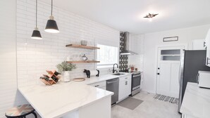 Una cocina moderna con armarios blancos, una isla central, iluminación colgante y un salpicadero blanco y negro.