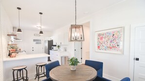 Una cocina moderna con armarios blancos, una isla central con taburetes, iluminación colgante y un cuadro abstracto y colorido en la pared.