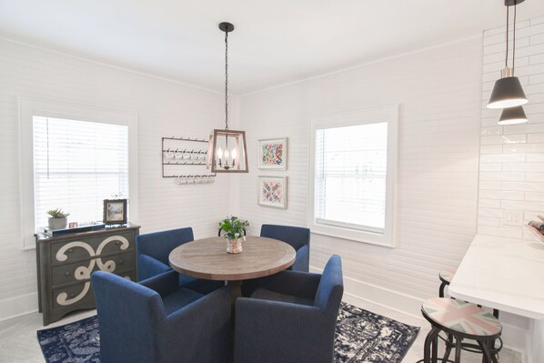 A dining area with a round wooden table surrounded by blue chairs, a chandelier, and framed artwork on the walls.