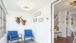 Een hal met twee blauwe stoelen, een witte muur met ingelijste foto’s, en een trap die naar een eetgedeelte leidt.