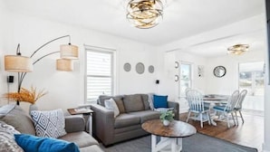 Een moderne woonkamer met een grijze bank, een salontafel en een eethoek met een witte tafel en stoelen.