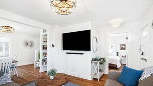 Een moderne woonkamer met een flatscreen televisie, houten vloeren en een eethoek met stoelen en een tafel.