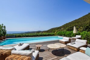 Un espace aménagé au bord de la piscine, avec des meubles en osier, une terrasse en bois et une vue sur la mer.