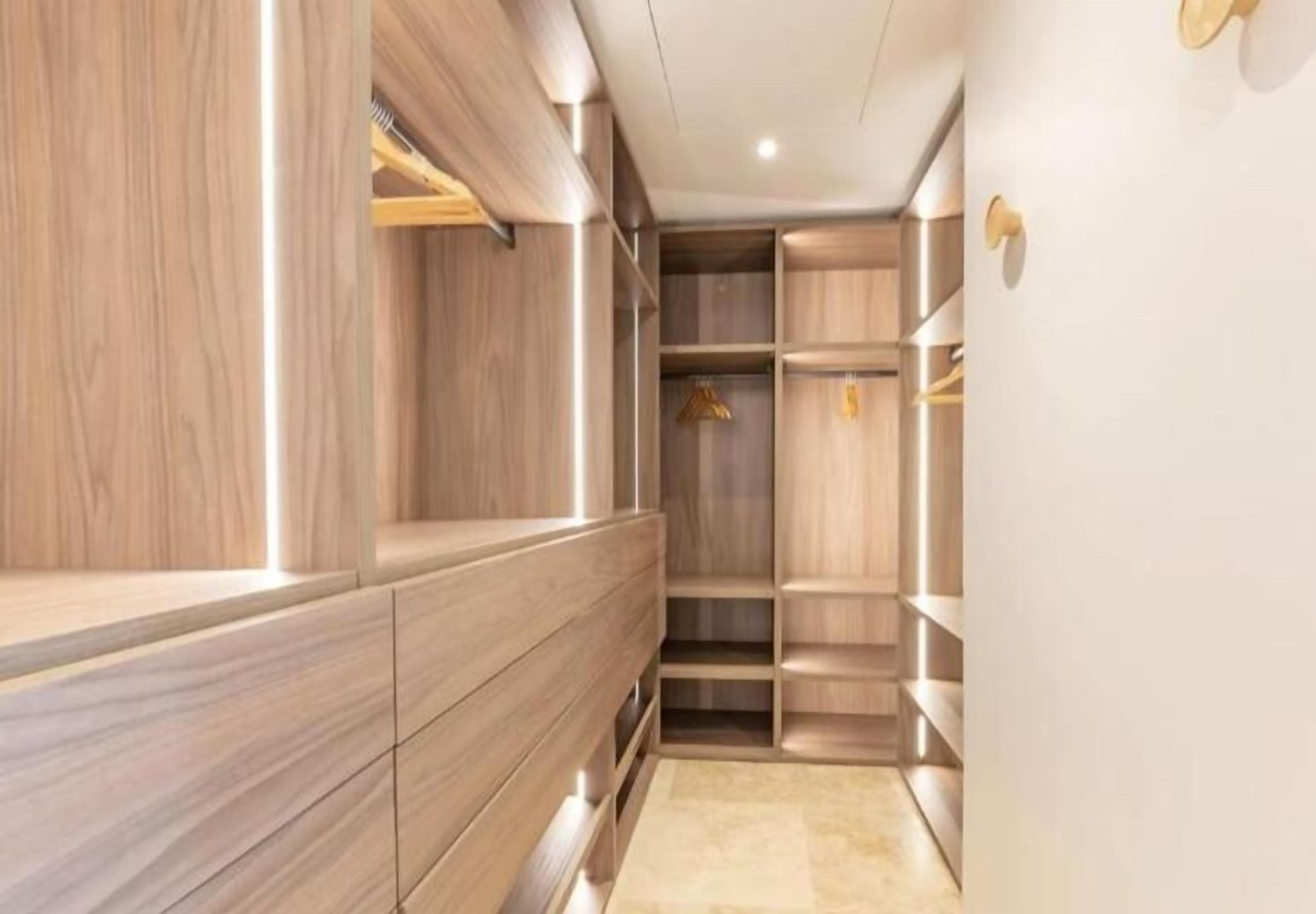 Un dressing moderne et bien éclair é, doté de meubles en bois et d’étagères intégrées.