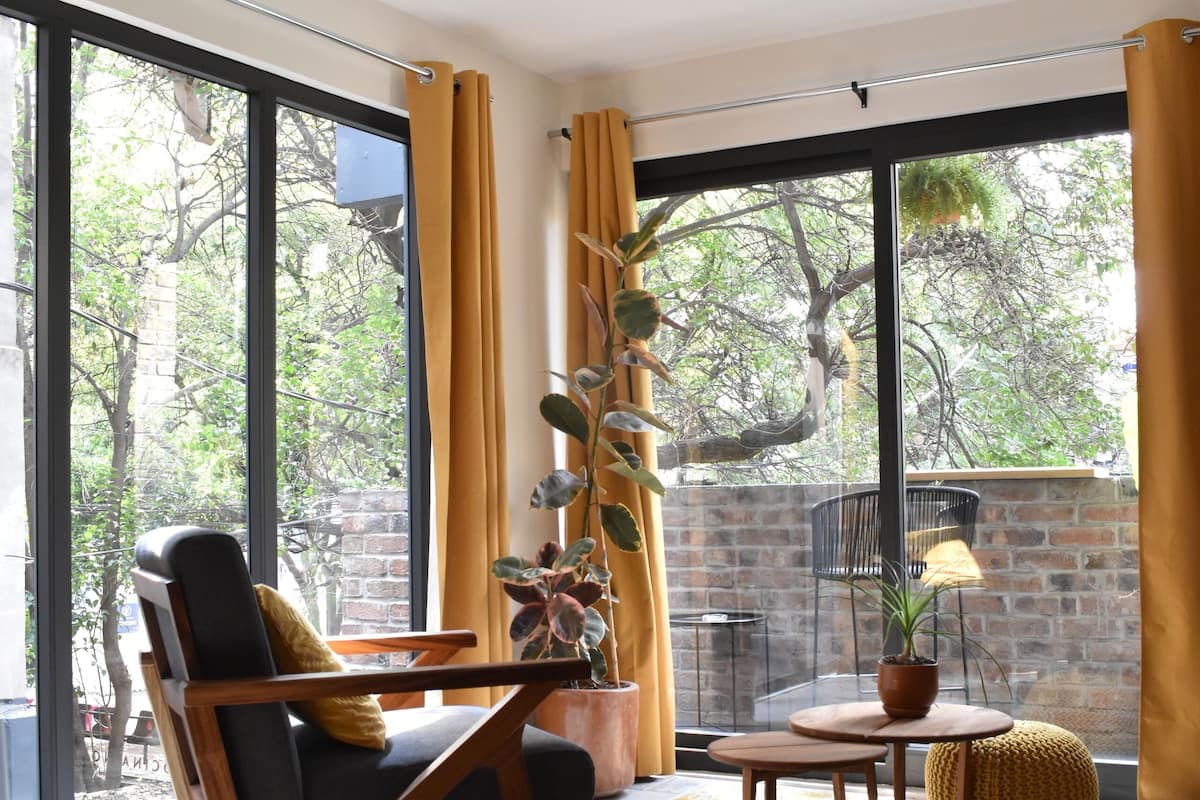 A modern living room with a large window, a wooden chair, a small table, and a potted plant.