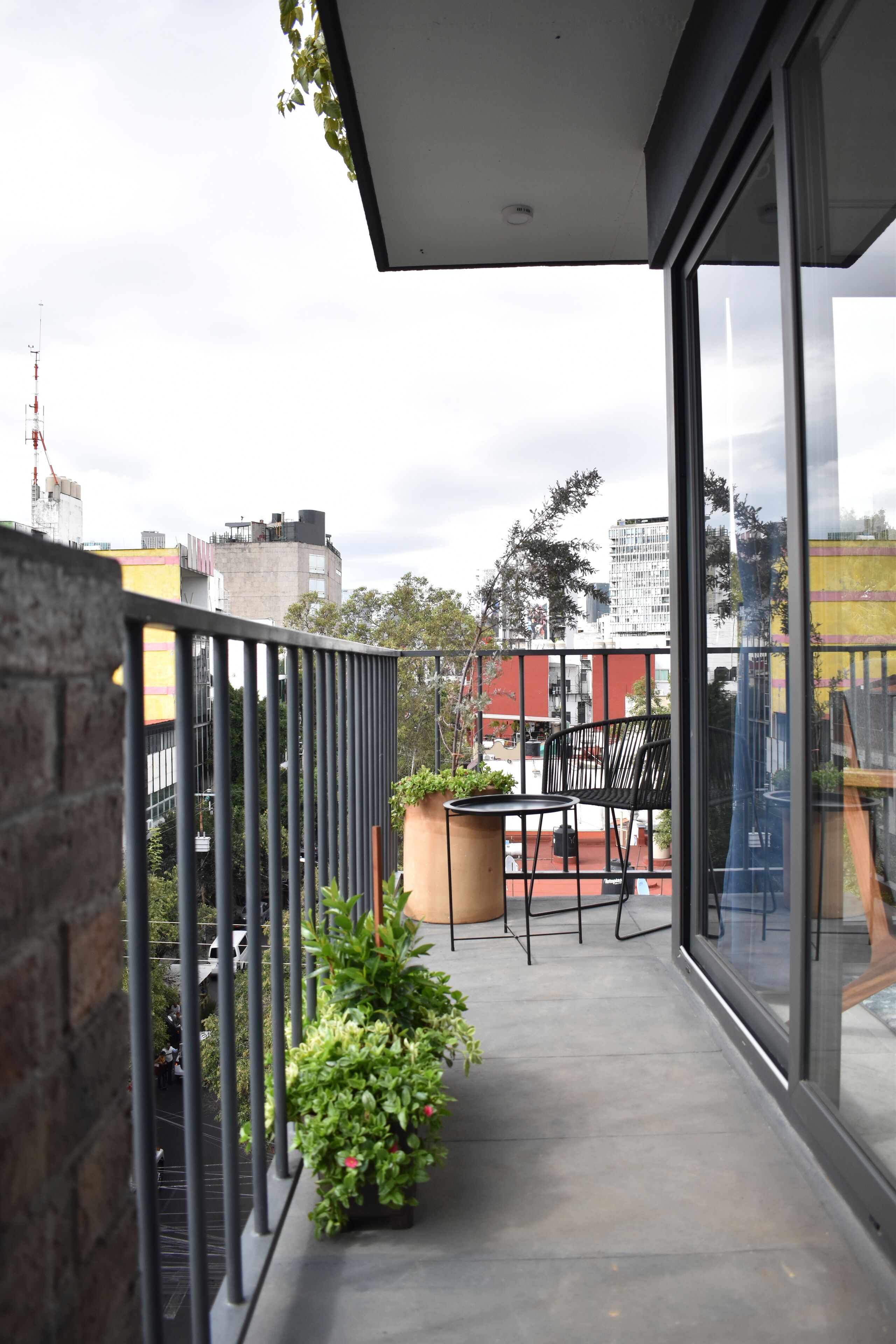 A balcony with a table and chairs, potted plants, and a view of the cityscape.