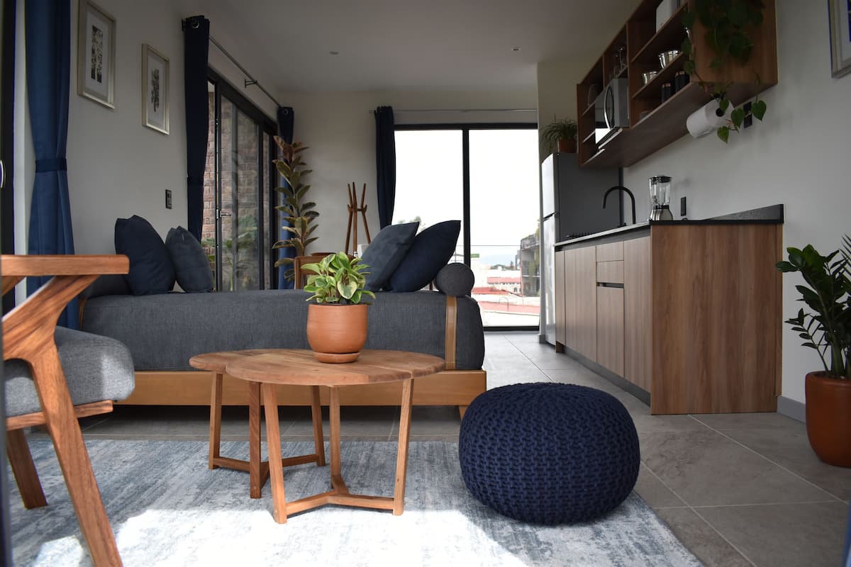 A modern living room with a sofa, a round wooden table, and a blue pouf.