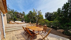 Un patio al aire libre con una mesa y sillas de madera, rodeado de formaciones rocosas y árboles.