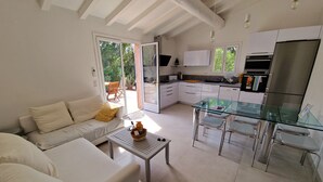 Una cocina moderna con armarios blancos y electrodomésticos de acero inoxidable, una mesa de comedor de vidrio y un sofá con un frutero.