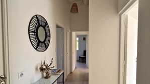 Un pasillo con una mesa consola de vidrio, un espejo decorativo y una lámpara de fibra trenzada.