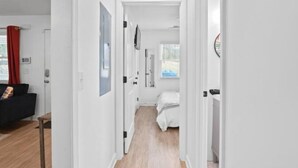 A narrow hallway leading to a bedroom with a bed, a small table, and a red curtain. - Luxe Modern 3BR Sleeps 6 by Atlantic Station (Atlanta)