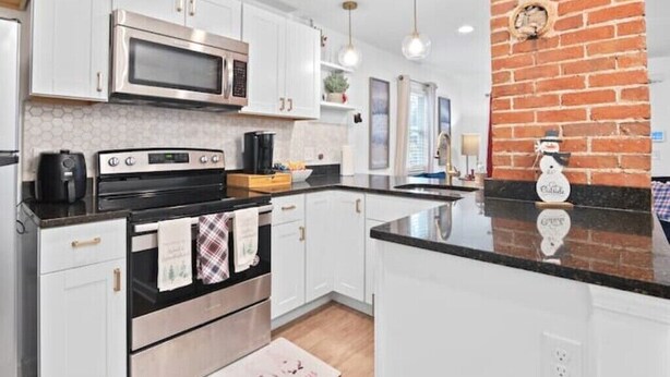 A modern kitchen with white cabinets, stainless steel appliances, and a black countertop. - Luxe Modern 3BR Sleeps 6 by Atlantic Station (Atlanta)