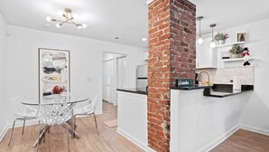 A modern kitchen with a brick accent wall, white cabinetry, and a dining area with a glass table and chairs. - Luxe Modern 3BR Sleeps 6 by Atlantic Station (Atlanta)