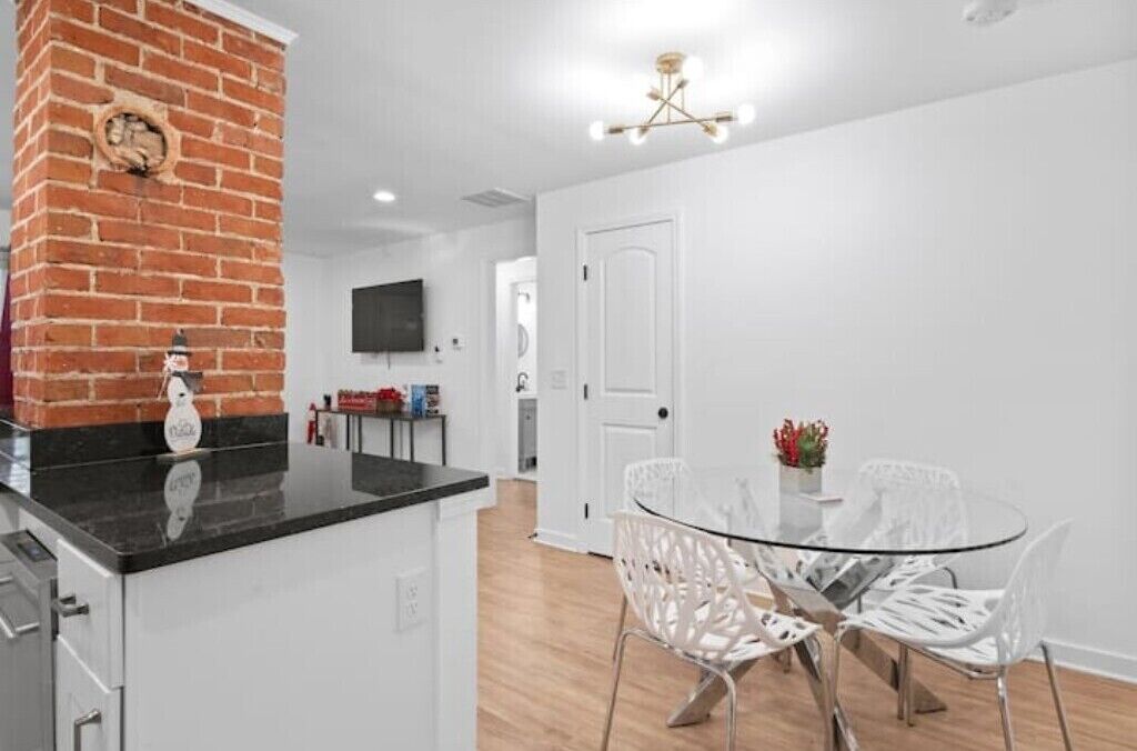 Una cocina moderna con una pared de ladrillo decorativa, una isla de vidrio, sillas blancas y una mesa de comedor.