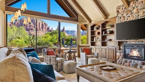 Ein geräumiges Wohnzimmer mit großem Fenster und Blick auf eine gebirgige Landschaft, inklusive Kamin und gemütlicher Sitzgelegenheiten.
