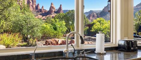 Una cocina con un lavamanos, un tostador y una ventana con vistas a un paisaje rocoso.