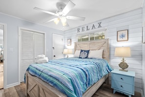 A bedroom with a bed, a nightstand, a ceiling fan, a wall-mounted sign, and a door. - Open concept, w/Covered Porch + Golf Cart (Myrtle Beach)