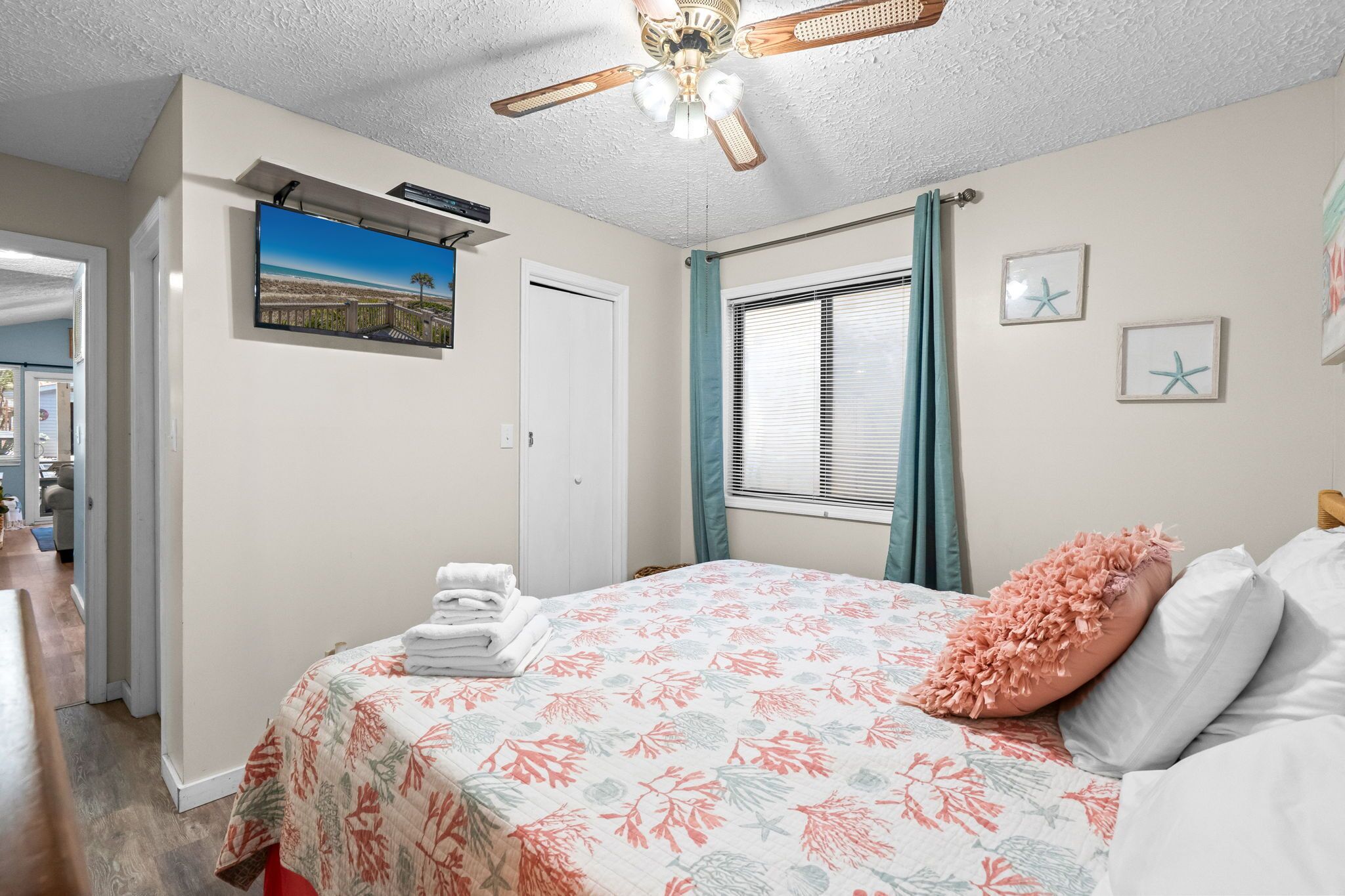 A bedroom with a bed, a ceiling fan, a window with curtains, and a wall-mounted TV.