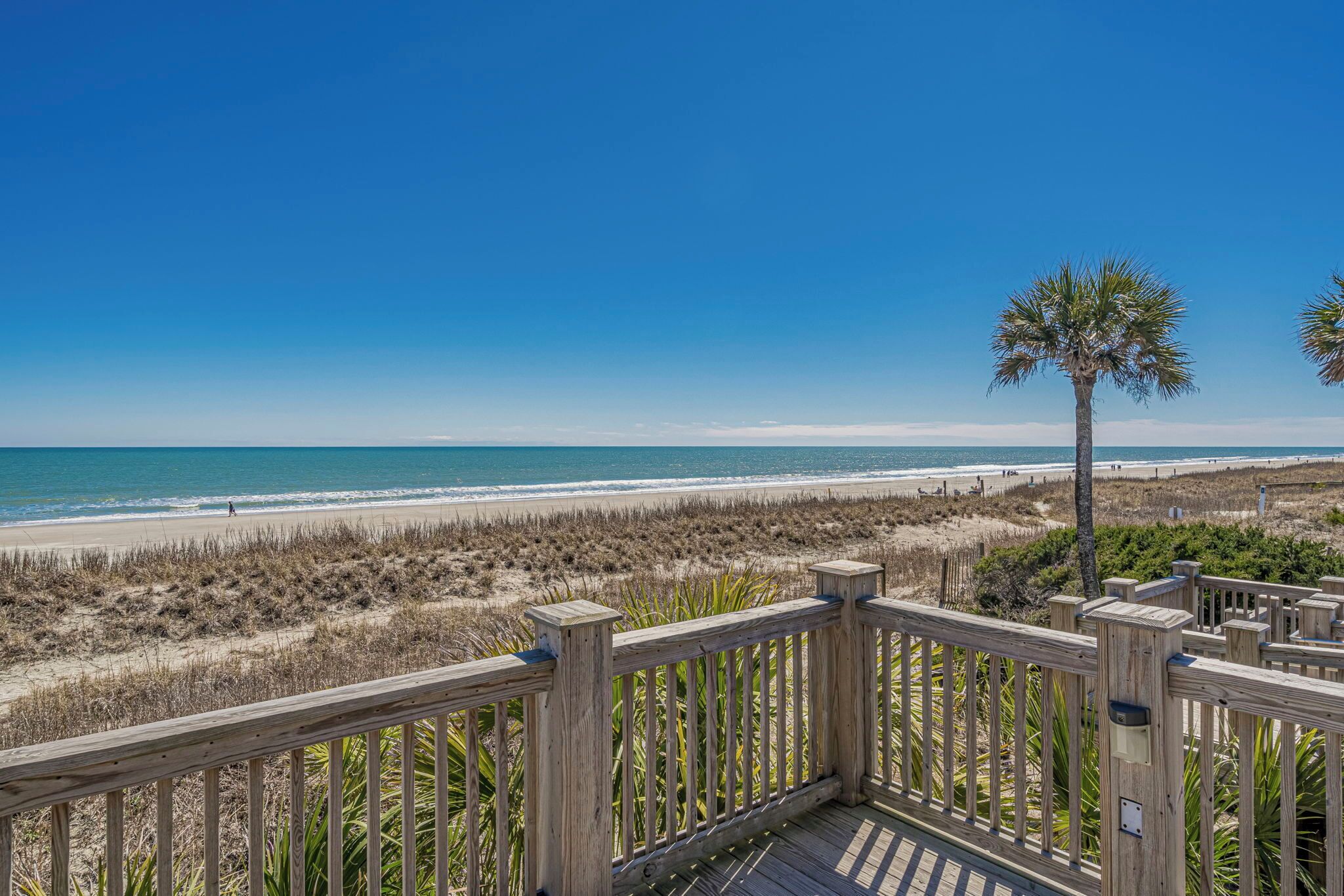 A wooden deck overlooking a beach with a clear blue sky.