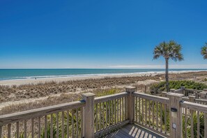 Eine Holzterrasse mit Blick auf einen Strand, der von einem klaren, blauen Himmel überdacht wird.