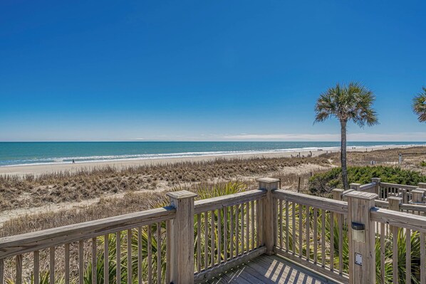 A wooden deck overlooking a beach with a clear blue sky.