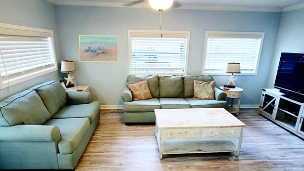 A living room with two sofas, a coffee table, a ceiling fan, and a television.