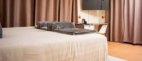 A hotel room with a large bed, a flat-screen TV mounted on the wall, and a desk with a chair.